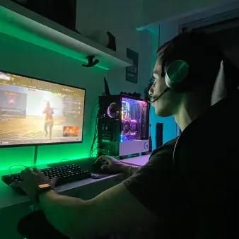 A user wearing headphones and a mic playing videogames on a monitor screen. 