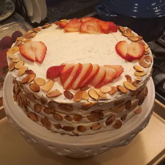A whole vanilla meringue cake with strawberries and sliced almond toppings. 