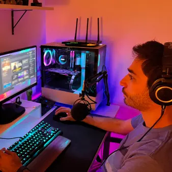 A user wearing headphones and using a microphone playing videogames on a monitor screen.