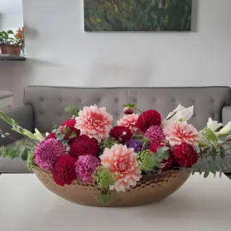 A large bouquet of multicolored flowers and eucalyptus in a bronze vase.