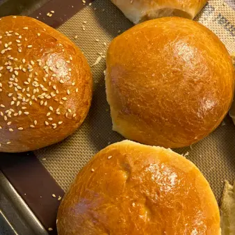 A close-up of three golden brioche buns with sesame seed toppings. 