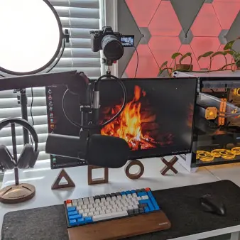 A desk set-up with two monitor screens, a microphone, headphones, keyboard, and lighting equipment. 